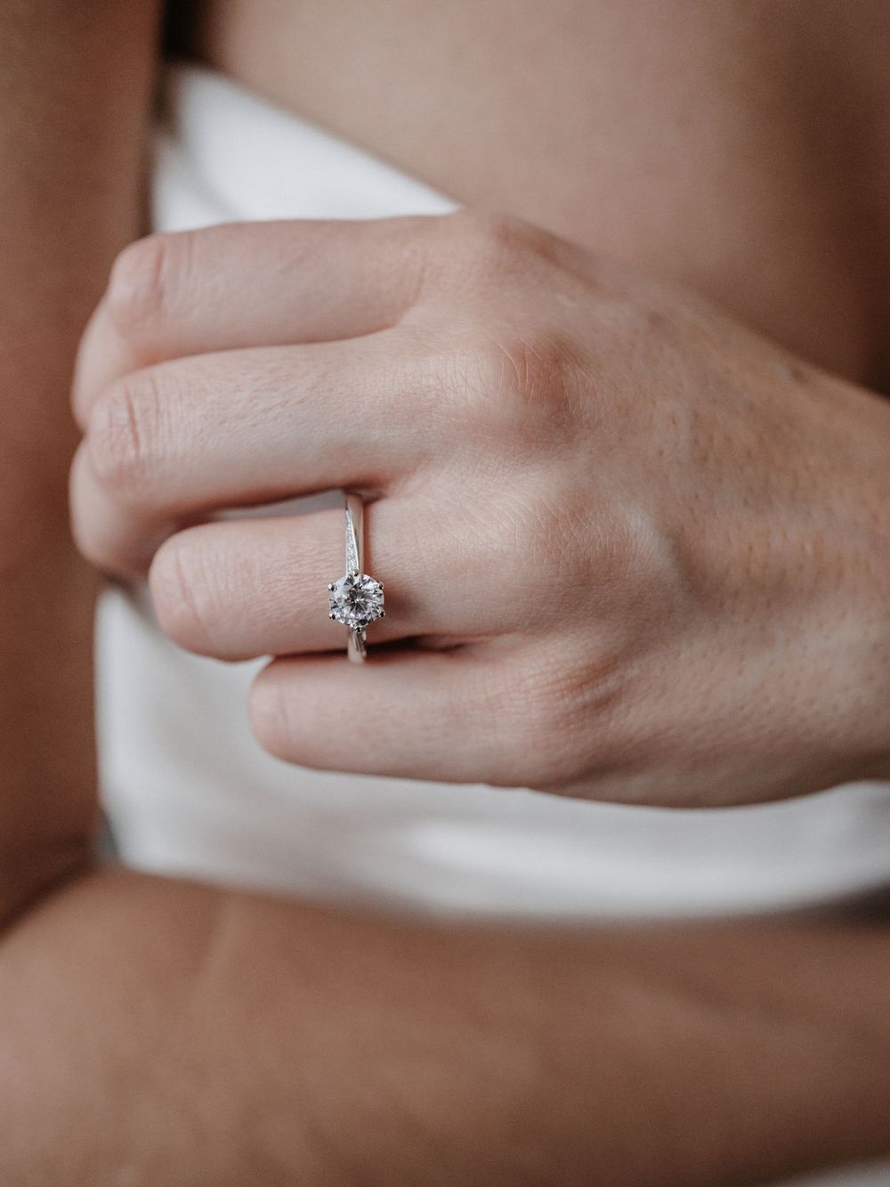 Hand mit Verlobungsring am weißen Kleid