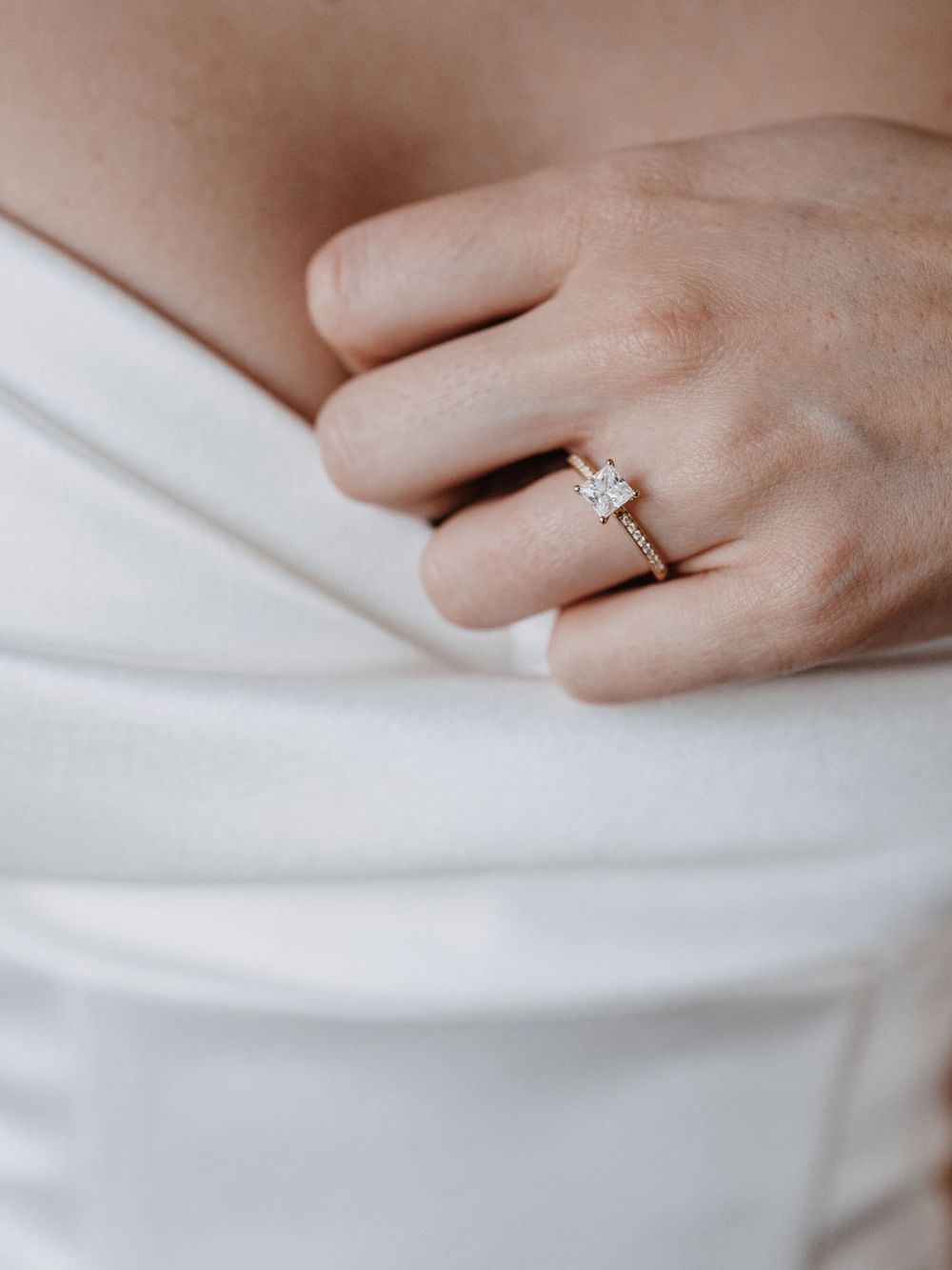 Hand mit Verlobungsring über dem weißen Kleid