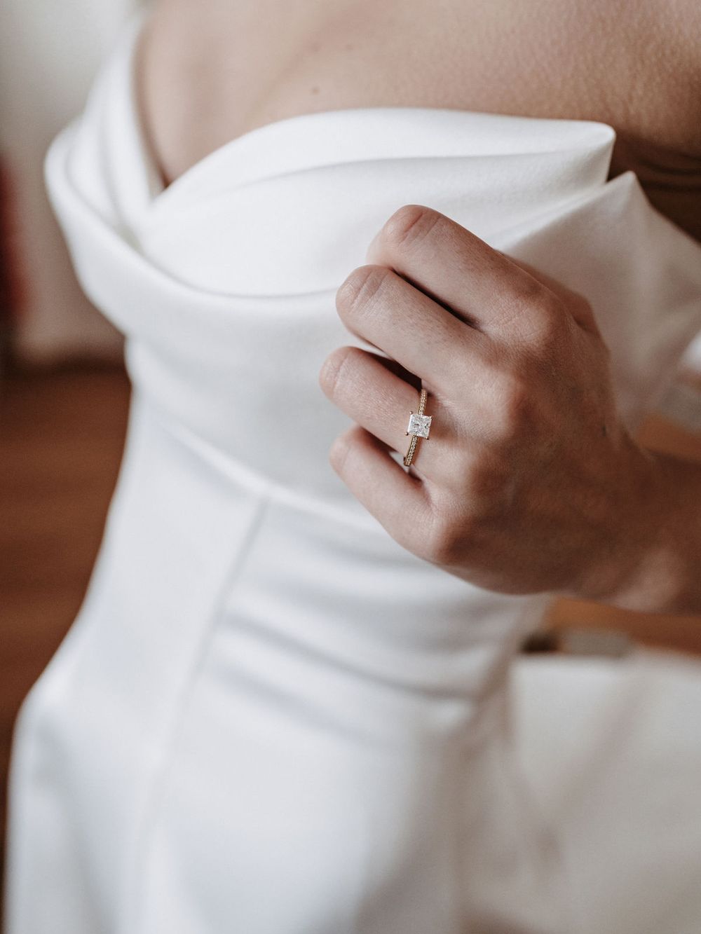 Hand mit Verlobungsring am Ausschnitt des Brautkleids
