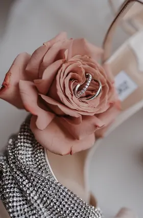 Trauringe auf einer rosafarbenen Rose neben Brautaccessoires