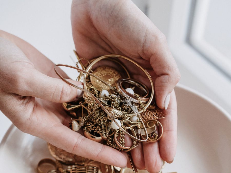 Zwei Hände halten eine Handvoll Altgold über einer weißen Schale mit Ketten und Ringen