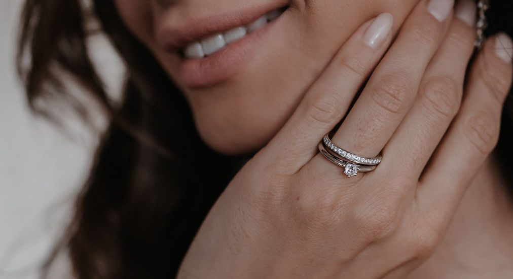 Braut lächelt und hält die Hand ans Gesicht, am Ringfinger ein Trauring mit Brillanten und ein schmaler Beisteckring
