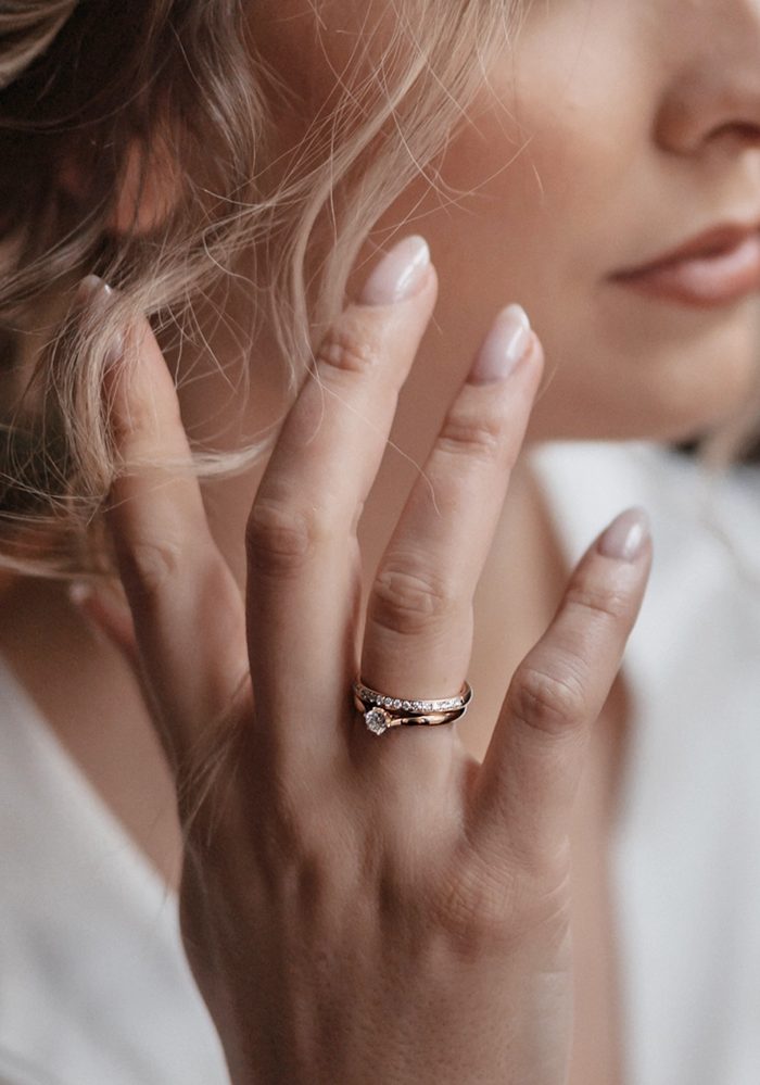 Frau hält die Hand ans Gesicht, am Ringfinger ein schmaler Trauring mit Brillanten