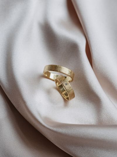 Zwei Trauringe aus Gelbgold mit strukturierter Oberfläche auf hellem Satin